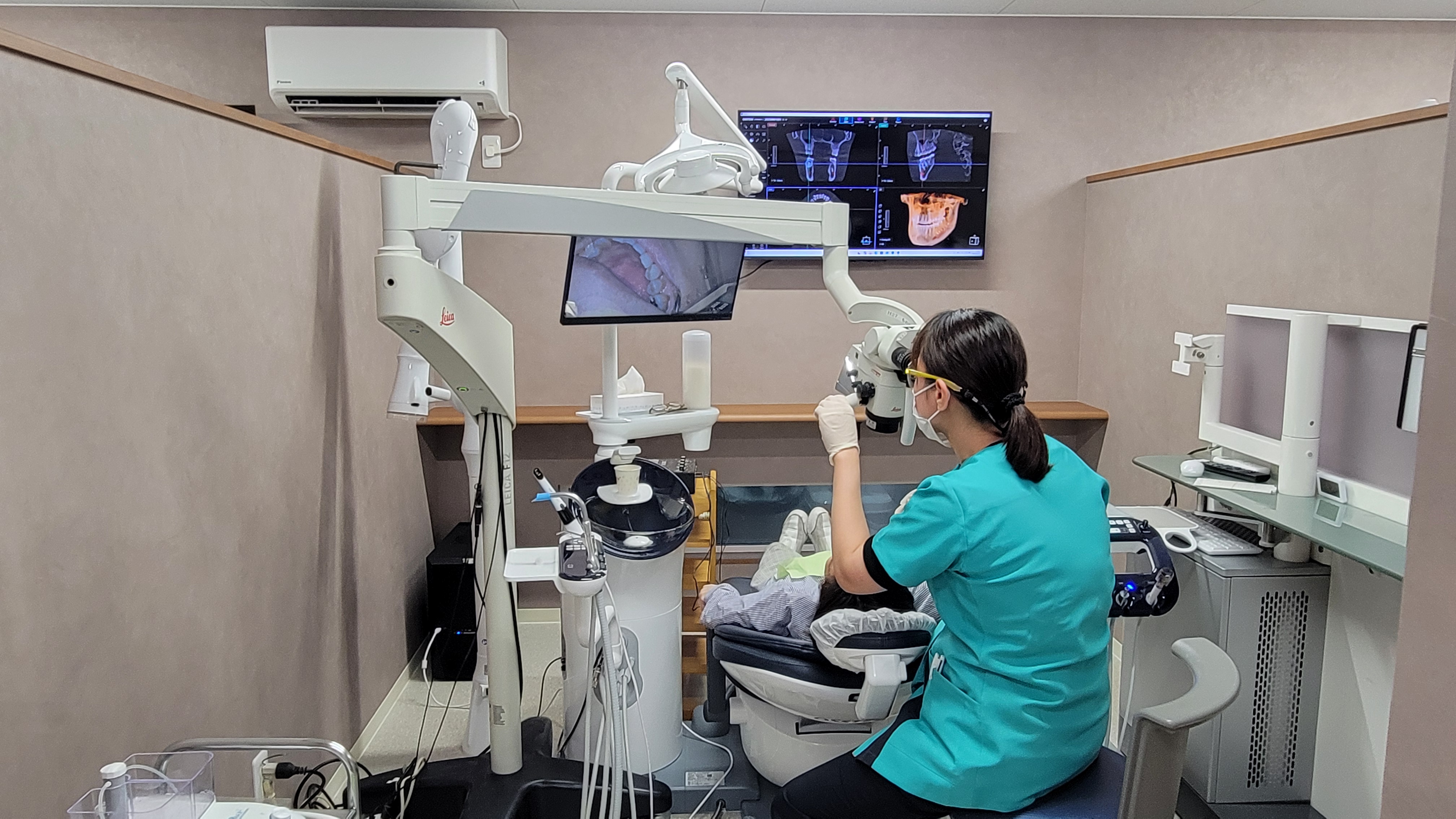 マイクロスコープとモニターに映るCT画像を併用し、口腔内の精密診療を行う女医の院長